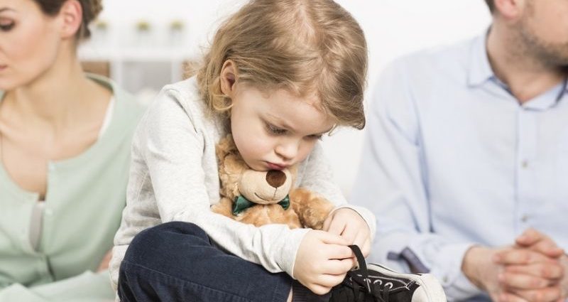 gloomy young family with a sad little boy hugging a teddy bear, and his parents with depressed looks